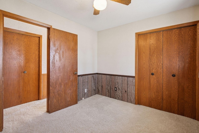 unfurnished bedroom with ceiling fan, carpet floors, a closet, and wood walls