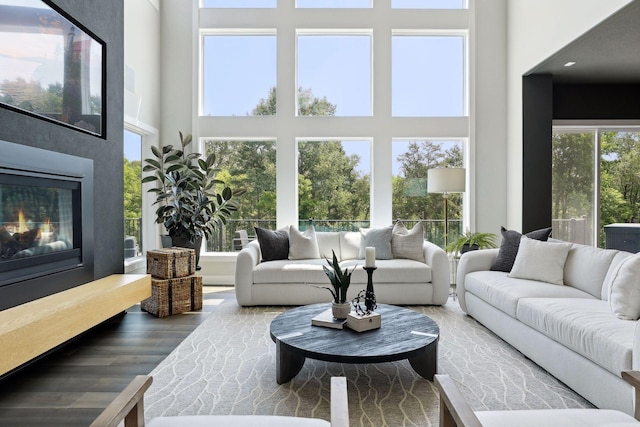 living room with a high end fireplace, wood-type flooring, and a towering ceiling