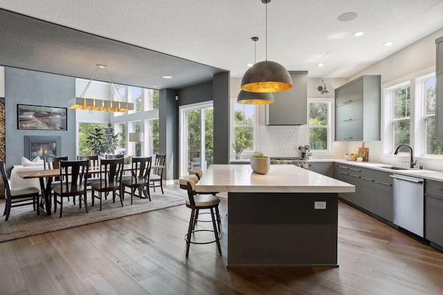 kitchen with a kitchen island, pendant lighting, gray cabinetry, hardwood / wood-style flooring, and stainless steel dishwasher