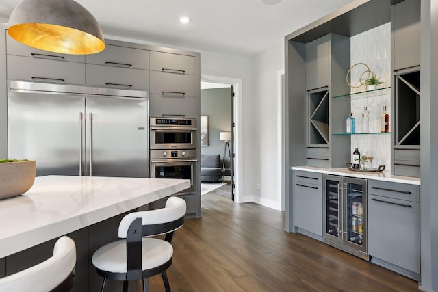 kitchen with gray cabinetry, appliances with stainless steel finishes, dark hardwood / wood-style floors, a kitchen breakfast bar, and beverage cooler