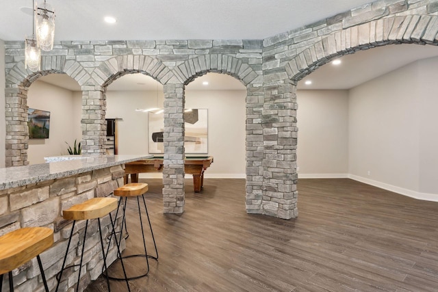 bar with ornate columns, dark wood-type flooring, light stone counters, and decorative light fixtures