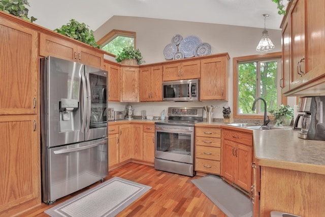 kitchen featuring lofted ceiling, decorative light fixtures, light wood-type flooring, and appliances with stainless steel finishes