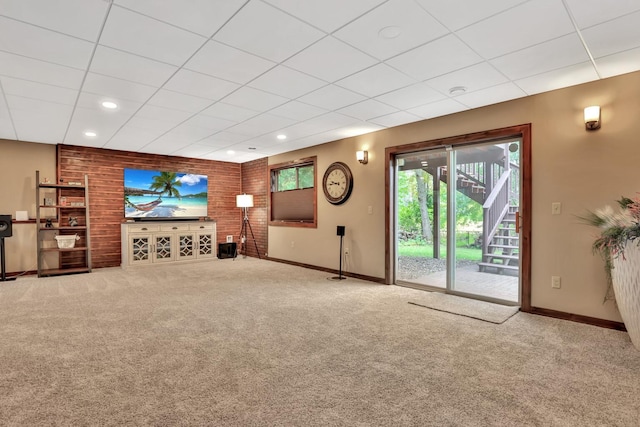 unfurnished living room featuring a drop ceiling, brick wall, and carpet