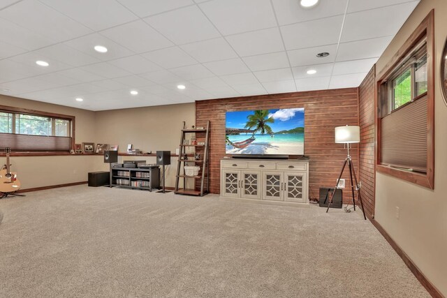 carpeted living room with a drop ceiling and wood walls