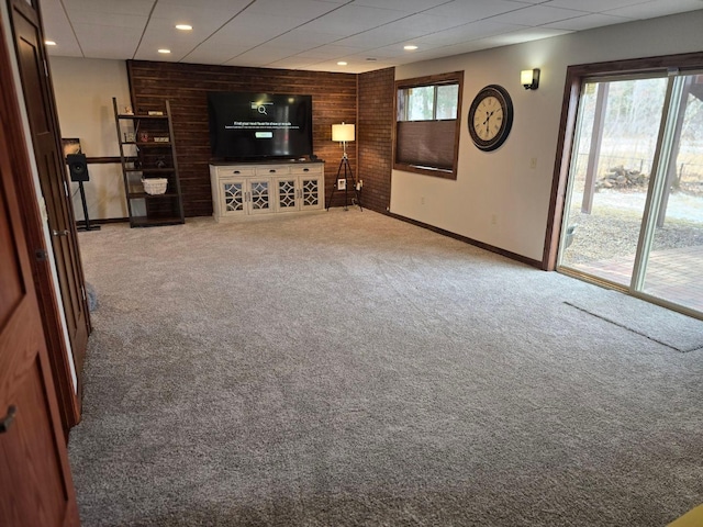 unfurnished living room with brick wall, a healthy amount of sunlight, and carpet flooring