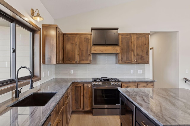 kitchen featuring lofted ceiling, sink, stainless steel range with gas stovetop, stone counters, and backsplash