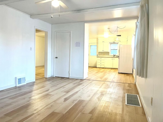 empty room featuring beamed ceiling, sink, ceiling fan, and light hardwood / wood-style flooring