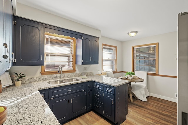 kitchen with sink, light stone counters, light wood-type flooring, and kitchen peninsula