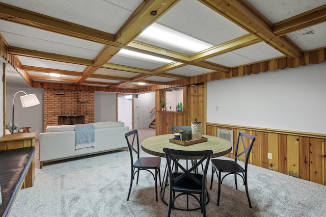 carpeted dining room featuring beamed ceiling, a brick fireplace, coffered ceiling, and wooden walls