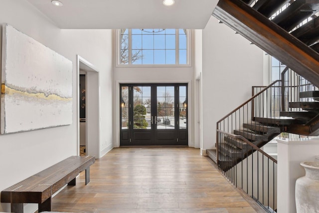 foyer with french doors, a towering ceiling, and light wood-type flooring