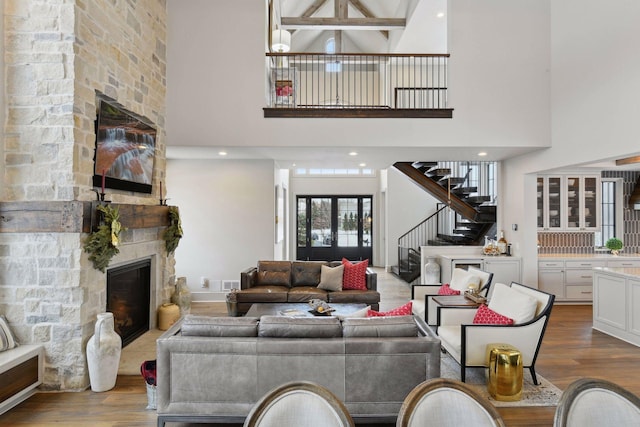 living room with hardwood / wood-style flooring, a towering ceiling, and a stone fireplace