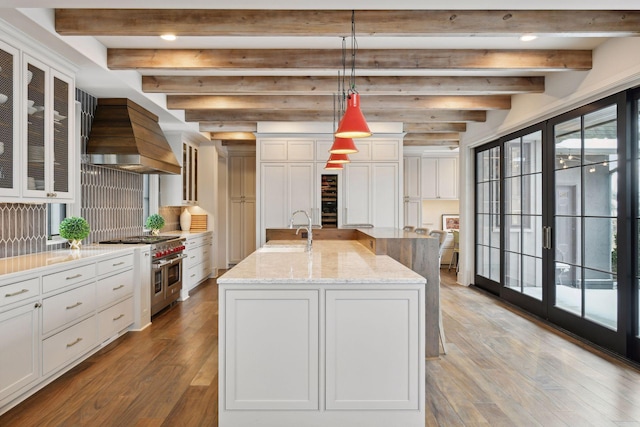 kitchen with sink, double oven range, an island with sink, custom range hood, and pendant lighting