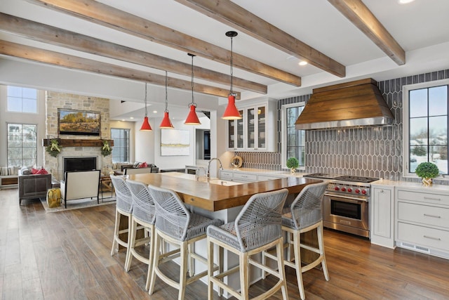 kitchen featuring premium range hood, pendant lighting, white cabinetry, sink, and designer stove