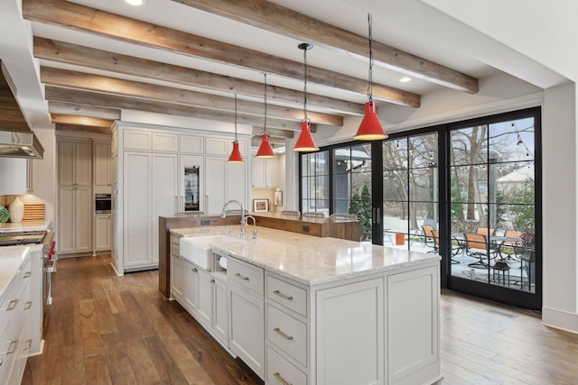 kitchen with a large island, sink, white cabinetry, hanging light fixtures, and light stone countertops