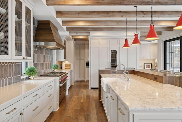 kitchen with pendant lighting, white cabinetry, custom range hood, a large island with sink, and range with two ovens