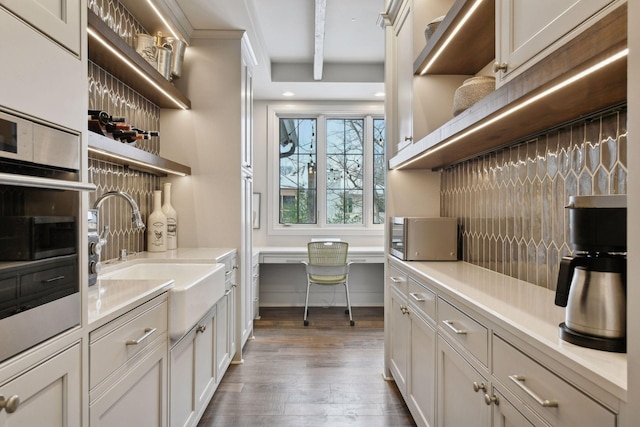 kitchen featuring appliances with stainless steel finishes, built in desk, sink, light hardwood / wood-style floors, and beam ceiling