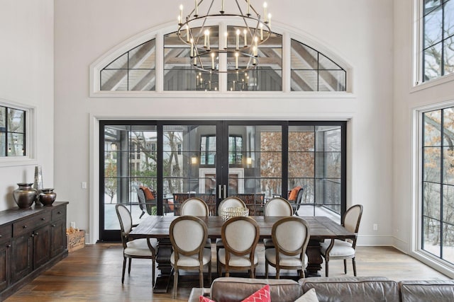 dining area featuring hardwood / wood-style flooring, a towering ceiling, and an inviting chandelier