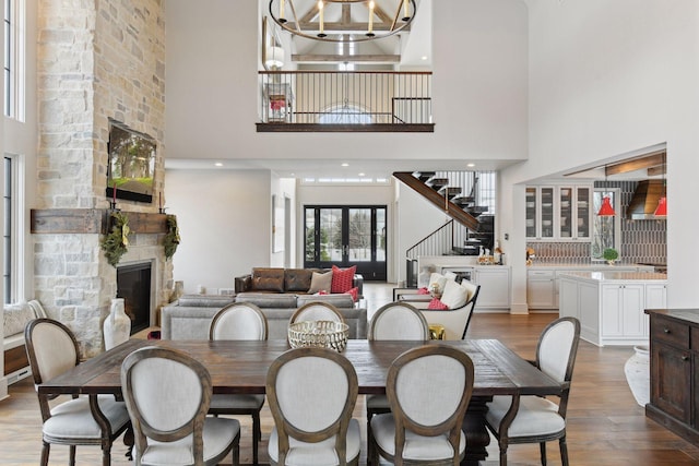 dining area with a stone fireplace, a towering ceiling, wood-type flooring, a chandelier, and french doors