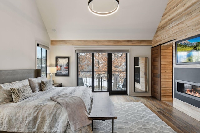 bedroom with high vaulted ceiling, a barn door, hardwood / wood-style floors, and a fireplace