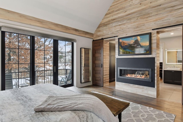 bedroom with high vaulted ceiling, a barn door, and light hardwood / wood-style floors