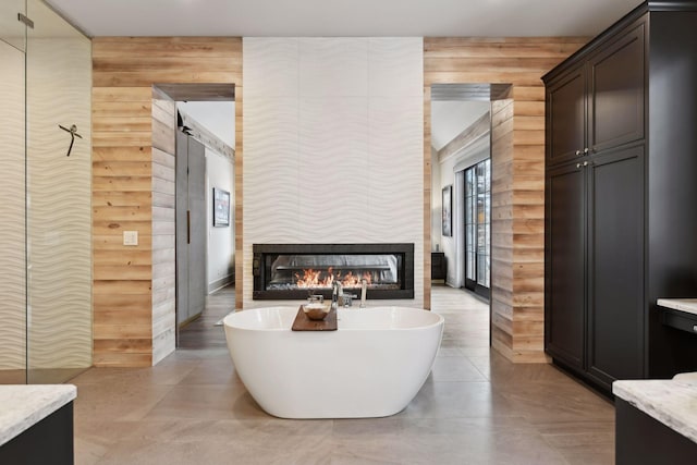 bathroom featuring a multi sided fireplace, vanity, wooden walls, and a bathing tub