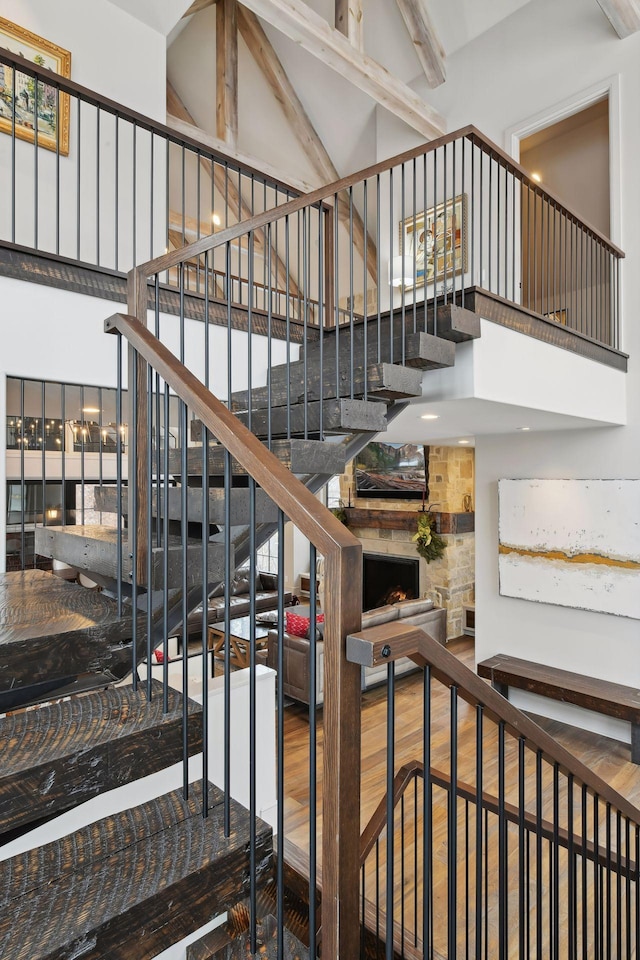 stairway featuring beamed ceiling, wood-type flooring, a towering ceiling, and a large fireplace