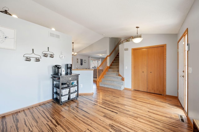 foyer with light wood-style floors, stairs, vaulted ceiling, and visible vents
