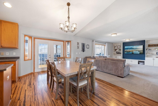 dining area featuring french doors, light wood-type flooring, baseboards, lofted ceiling, and an inviting chandelier