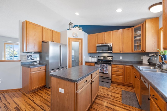kitchen featuring dark countertops, appliances with stainless steel finishes, a sink, light wood-style flooring, and a kitchen island
