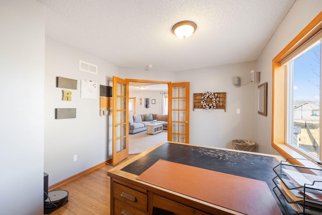 home office featuring light wood finished floors, a textured ceiling, french doors, baseboards, and visible vents
