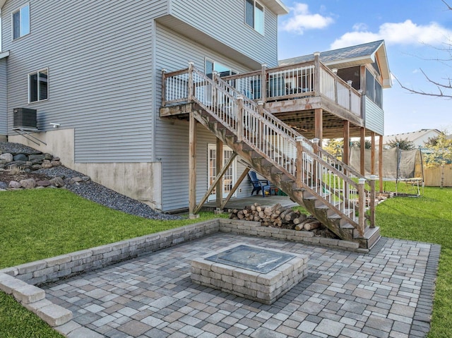 rear view of house with a trampoline, a wooden deck, stairway, a patio area, and a fire pit