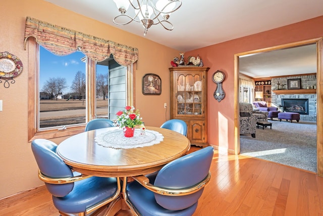 dining space with a stone fireplace, a chandelier, and light hardwood / wood-style flooring