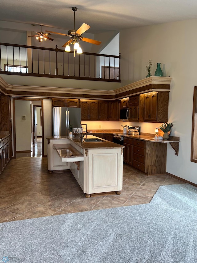 kitchen featuring high vaulted ceiling, a kitchen island with sink, stainless steel appliances, a sink, and baseboards