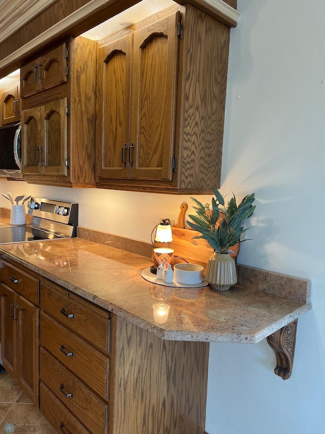 kitchen featuring light countertops, appliances with stainless steel finishes, tile patterned flooring, and brown cabinets