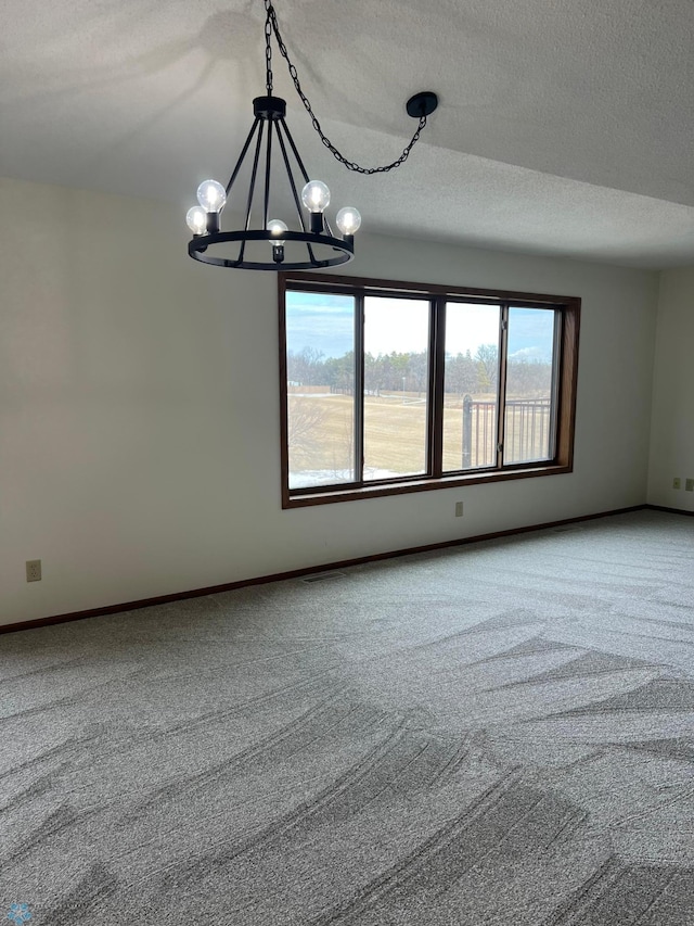 empty room featuring an inviting chandelier, a textured ceiling, baseboards, and carpet flooring