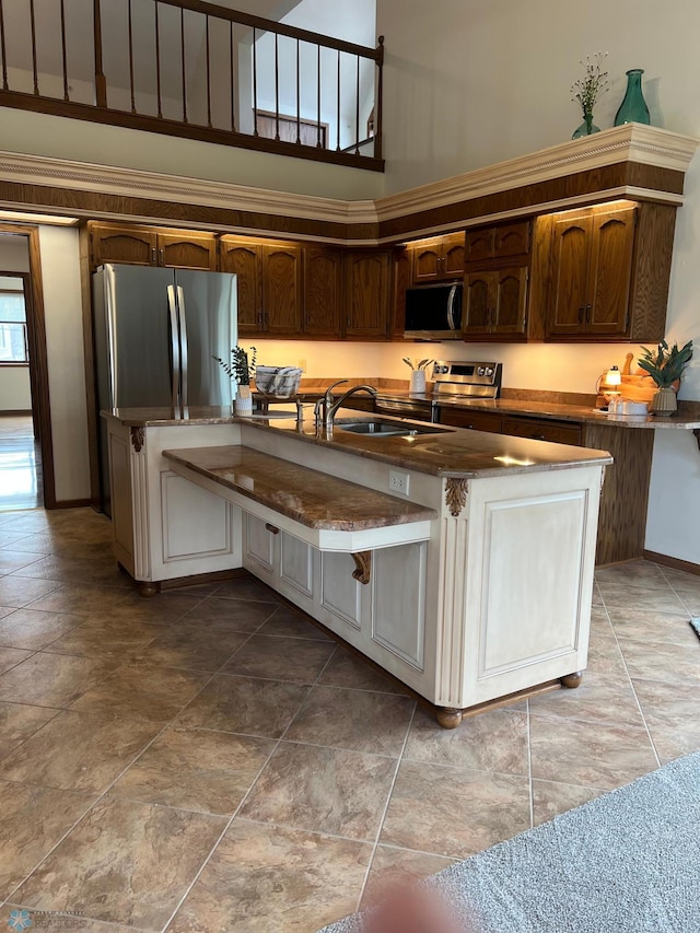 kitchen featuring a towering ceiling, dark countertops, a breakfast bar area, stainless steel appliances, and a sink