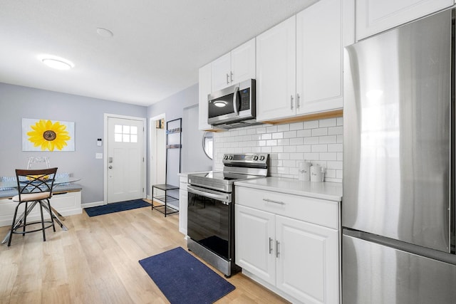 kitchen with tasteful backsplash, stainless steel appliances, light wood-type flooring, and white cabinets