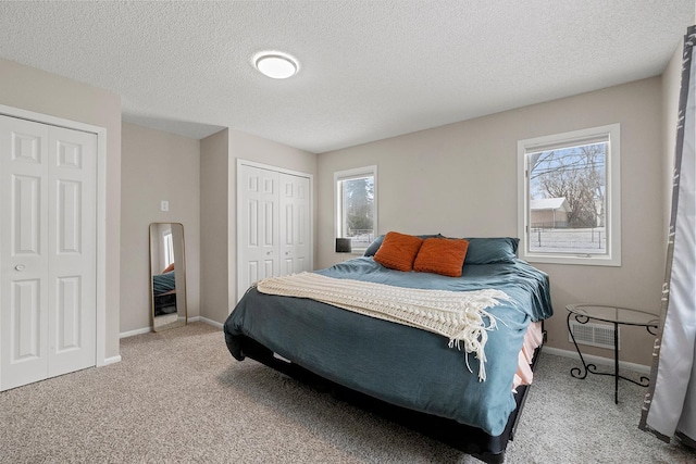 bedroom featuring a textured ceiling, carpet, multiple windows, and two closets