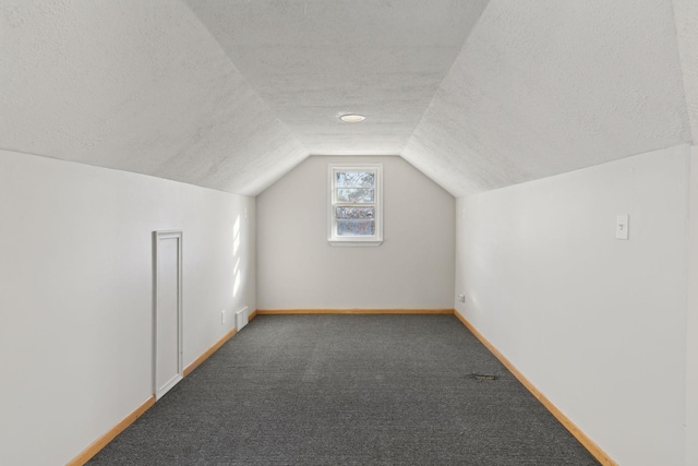 additional living space featuring dark colored carpet, vaulted ceiling, and a textured ceiling