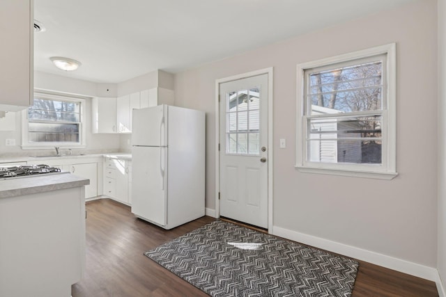 kitchen with white refrigerator, dark wood-type flooring, sink, and white cabinets