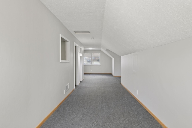 hallway with vaulted ceiling, a textured ceiling, and dark colored carpet