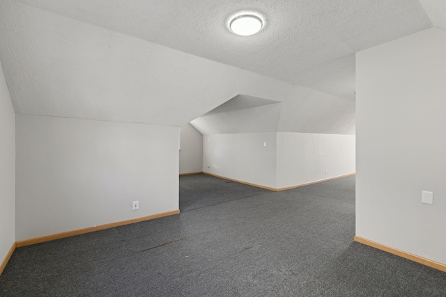 additional living space featuring vaulted ceiling, a textured ceiling, and dark colored carpet