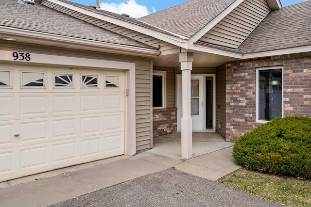 entrance to property featuring brick siding, an attached garage, and a shingled roof