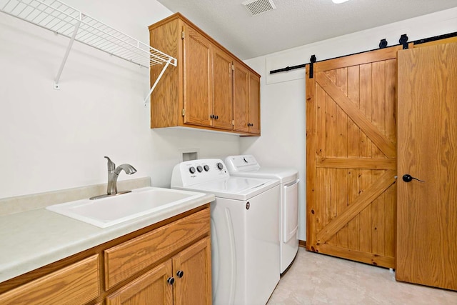 laundry room featuring visible vents, washer and clothes dryer, a barn door, a sink, and cabinet space