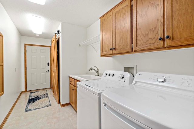 laundry room featuring baseboards, a barn door, a sink, cabinet space, and independent washer and dryer