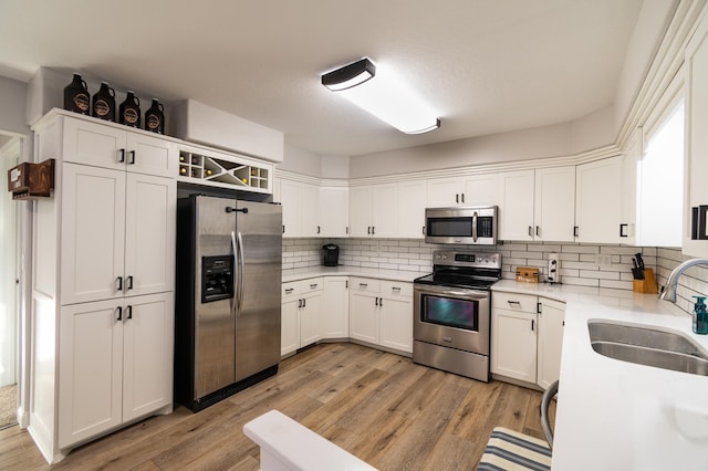 kitchen with appliances with stainless steel finishes, white cabinetry, sink, decorative backsplash, and light hardwood / wood-style floors