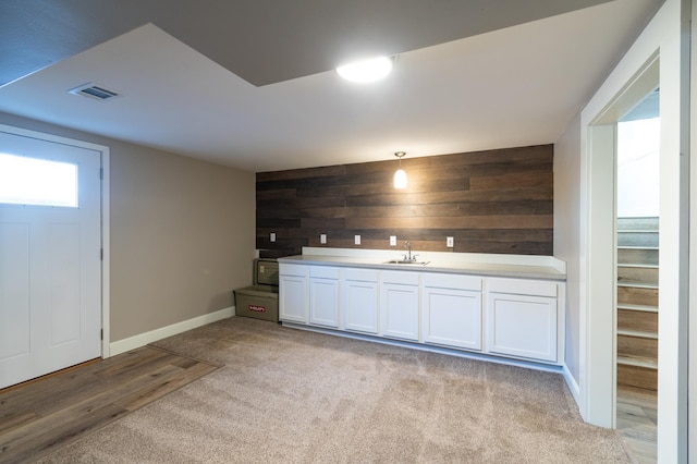 bar with sink, hanging light fixtures, white cabinets, light carpet, and wood walls