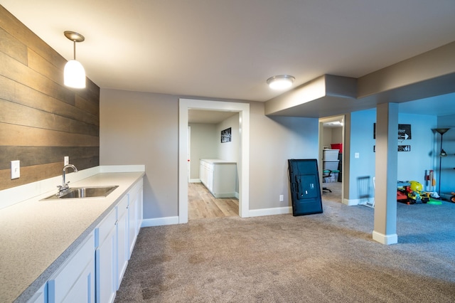 kitchen with sink, wooden walls, white cabinets, light carpet, and decorative light fixtures