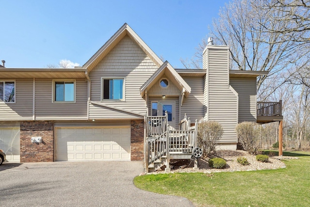 view of front facade with a front lawn, driveway, a chimney, brick siding, and an attached garage