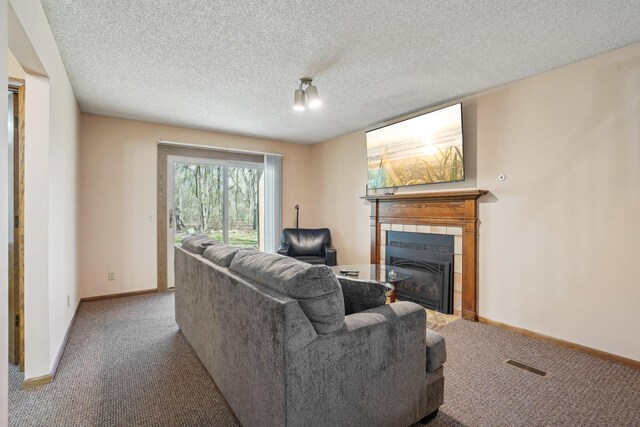living room featuring carpet flooring, a textured ceiling, baseboards, visible vents, and a tile fireplace